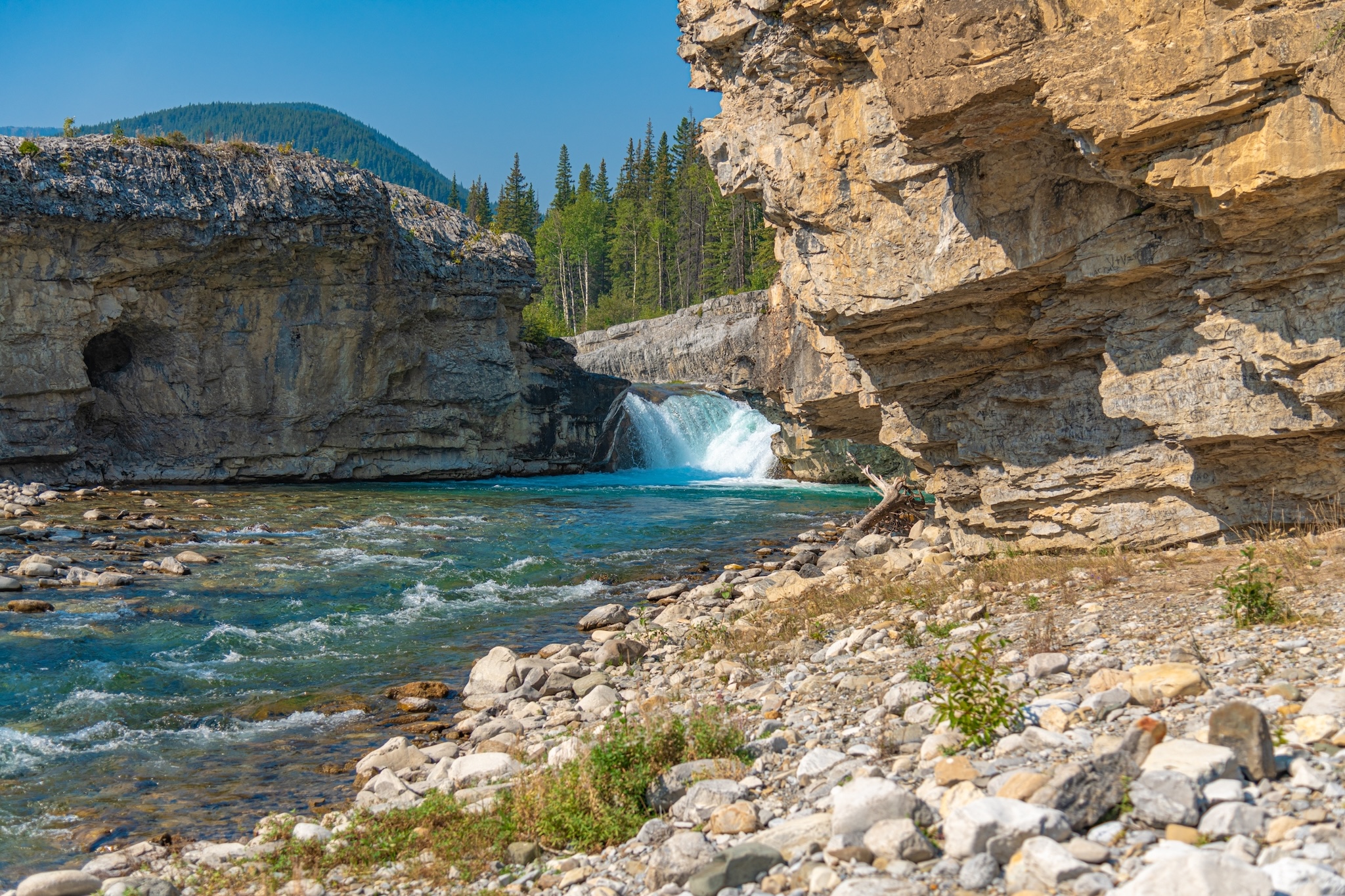 Scenic summer landscape of Elbow Falls in Kananaskis Country, Alberta, Canada. Beautiful waterfall cascading over rocky cliffs into the Elbow River with evergreen pine forest and blue sky in the Canadian Rocky Mountains.