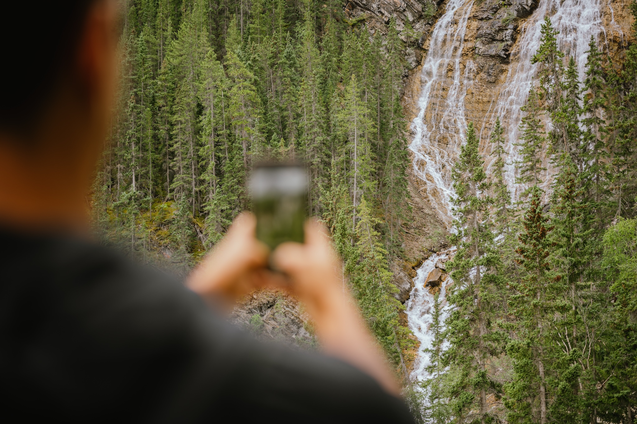 Person photographing a waterfall at Grassi Lakes trailhead, Canmore